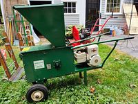Side view showing the green rectangular feed hopper and chute, black handles, and wheels of the Mighty Mac compost shredder grinder.