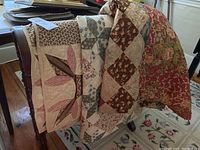 Three vintage quilts draped over wooden quilt rack visible, showing multiple patterns and colors