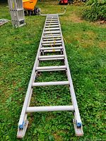 Long view of aluminum extension ladder layed on grass showing full length and stabilizer attachment at base with rope tied around rungs.