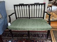 Front view of antique wooden bench with green upholstery and carved backrest