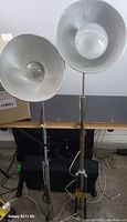 Two camera lighting units with large reflectors mounted on adjustable metal stands placed on floor