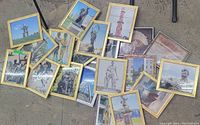 Full overview photo showing all 20 framed art prints scattered on ground, mostly in gold-tone frames with various photos and prints depicting statues and monuments.