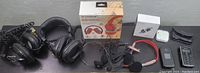 Overview of all lot items laid out on table including headphones, earbuds in charging case, wireless boxed headphones, smartphones, cables.