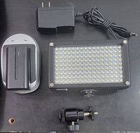 Top view showing battery charger dock with battery slot, Lumahawk power adapter, LED panel light, and adjustable mounting adapter.