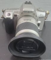 Front angle of Minolta STSi Maxxum camera with attached lens and lens hood, showing Minolta branding on lens cap and camera body.