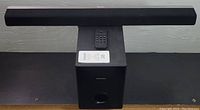 Philips black speaker bar and subwoofer showing front angle with remote on top of the subwoofer
