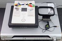 Top view of Sony DAV-DZ120 DVD player with accessories on top, including the white remote control, manuals, and the square loop antenna.