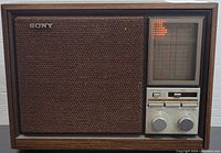 Front view showing SONY branded tabletop radio with woven speaker grille and tuning window illuminated by orange lights.