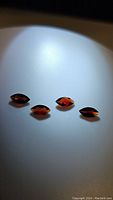 Four marquis cut almandine garnet gemstones with orange-red coloration on white background.