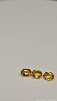 Three oval shaped canary yellow sapphires placed side by side on white background, showing facets and color vibrancy.