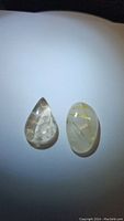 Two clear quartz gemstones with golden rutile inclusions, pear and oval shapes.