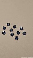 Top view of about 10 round blue sapphires laid out on beige surface, showing size and color.