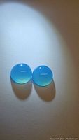Close up photo showing the matched pair of icey blue chalcedony cabochon gemstones with a polished, glossy surface under light source.