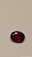 Close-up of an oval cut natural blood red ruby gemstone showing vivid deep red color and faceted polished surface.