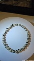 Natural dalmatian jasper bead bracelet displayed in a circular shape under light, showing pattern and color of beads.