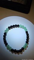 Top-down view of natural green aventurine and jet black onyx bead stretch bracelet arranged in a circular shape, showcasing bead color and texture.