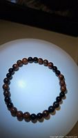 Full view of the stretchy bracelet formed with mahogany jasper and black onyx beads laid flat on a white surface under soft light showing the bead colors and size.