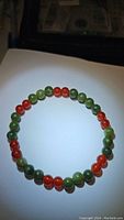 Image showing natural gemstone bracelet made of green jade and fire orange carnelian beads in a circle on a white background.