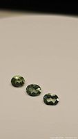Three oval cut green apatite gemstones displayed in a row showing facets and clarity under light.