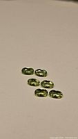Six oval-shaped natural Peridot gemstones, bright apple green color, laid out on a plain background.