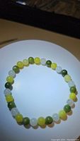 Photo of natural jade bead bracelet showing round polished beads in green, lemon yellow, and white colors on white background.