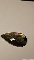 Photo of pear-shaped cabochon checkerboard cut labradorite gemstone showing natural labradorescence and facets