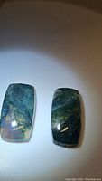 Photo showing two natural moss agate cabochons with green moss-like internal inclusions and polished surface.
