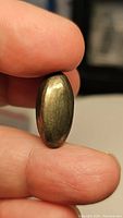 Close-up image showing the golden metallic surface, oval shape, and polished cabochon cut of the pyrite gemstone.