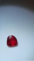 Close-up photo of a pear-shaped, blood red ruby gemstone showing surface polish and internal clarity under natural light.