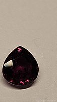 Close-up photo of a pear shaped deep purple sapphire gemstone, showing facets and color saturation under ambient light.