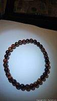 Top view of a stretchy bracelet composed of round polished red tigerseye beads placed in a circular shape on white background.