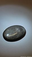 Oval polished cabochon silver sheen obsidian stone on plain background showing its sheen and shape