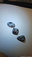 Three unique natural snowflake obsidian cabochons displayed on a white surface under lighting highlighting their pattern and polish.