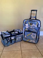 Photo shows both luggage pieces side by side on tile floor. Upright suitcase with handle extended and duffle bag placed horizontally.