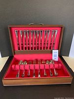 Full view of the wooden chest open showing all 60 pieces of cutlery arranged neatly inside on red cloth lining.