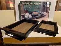 Two rectangular wood trays, one large and one small, with bamboo lining and dark wood frames, shown on a table with the original box behind.