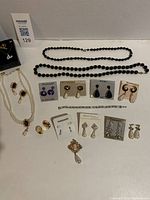 Photo showing entire lot of costume jewellery including necklaces, earrings on cards, brooches, and clip-ons arranged on a white surface.