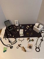 Wide view of assorted costume jewellery including necklaces, brooches, earrings, rings, and bracelets arranged on a purple cloth with white background.