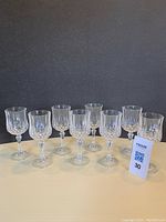Set of eight clear crystal wine glasses with a patterned design and faceted stems, arranged in a row against a black background.