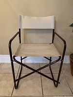 Front view of director's chair showing brown metal frame and beige canvas seat and backrest.