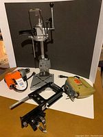 Four items including drill press stand support, orange electric drill, beige jigsaw, black Guidemate on white background