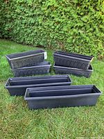 Photo of 6 black rectangular flower planters placed on grass including 2 large and 4 smaller sized planters without hangers.