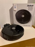Robot vacuum positioned in front of its original box showing front view and branding