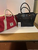 Two bags side by side showing overall size and condition: black Kensie leather purse and red PINK duffle bag.
