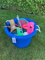 Large blue bucket filled with various outdoor play items and balls on grass
