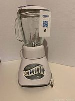 Full view of Oster blender with glass pitcher and electrical cord, showing the front design and measurement markings on pitcher.