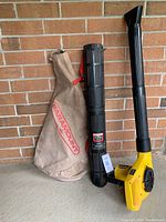 Paramount power blower with vacuum bag and blower tube positioned standing against brick wall, showing overall lot contents