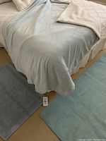 Blue throw blanket draped over bed with blue reversible bath mat and IKEA NASTVED rug laid on floor.