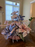 Full view of silk flower arrangement with rose and blue flowers in ceramic base on a wooden surface with window background