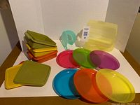 Tupperware storage containers in stack with lids laid out; assorted colorful IKEA plastic plates; translucent onion/tomato holder in front